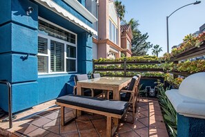 A patio with a wooden table and chairs, a blue wall, and a garden with various plants.