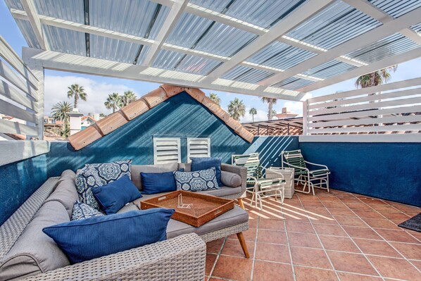 A covered outdoor seating area with a sofa, chairs, and a tray table. - Located in downtown O'side - Blue Jay by the Pier (Oceanside)