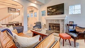 A spacious living room with a fireplace, a staircase, and a large TV mounted above it. - Located in downtown O'side - Blue Jay by the Pier (Oceanside)