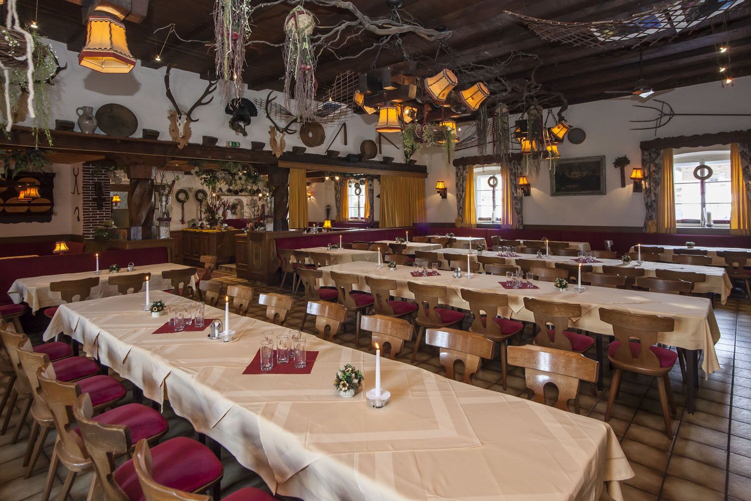A restaurant with multiple tables and chairs, decorated with hanging lanterns and wall-mounted animal heads.