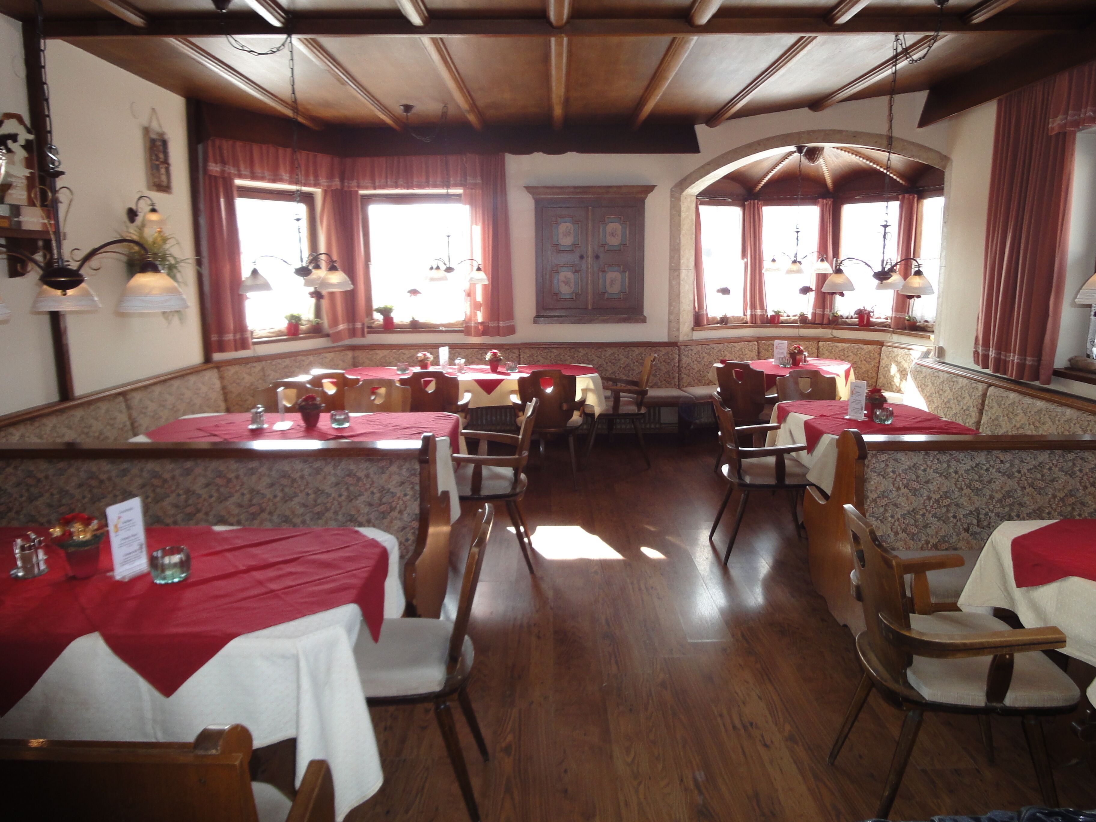 A restaurant with wooden tables and chairs, red tablecloths, and a classic interior design.