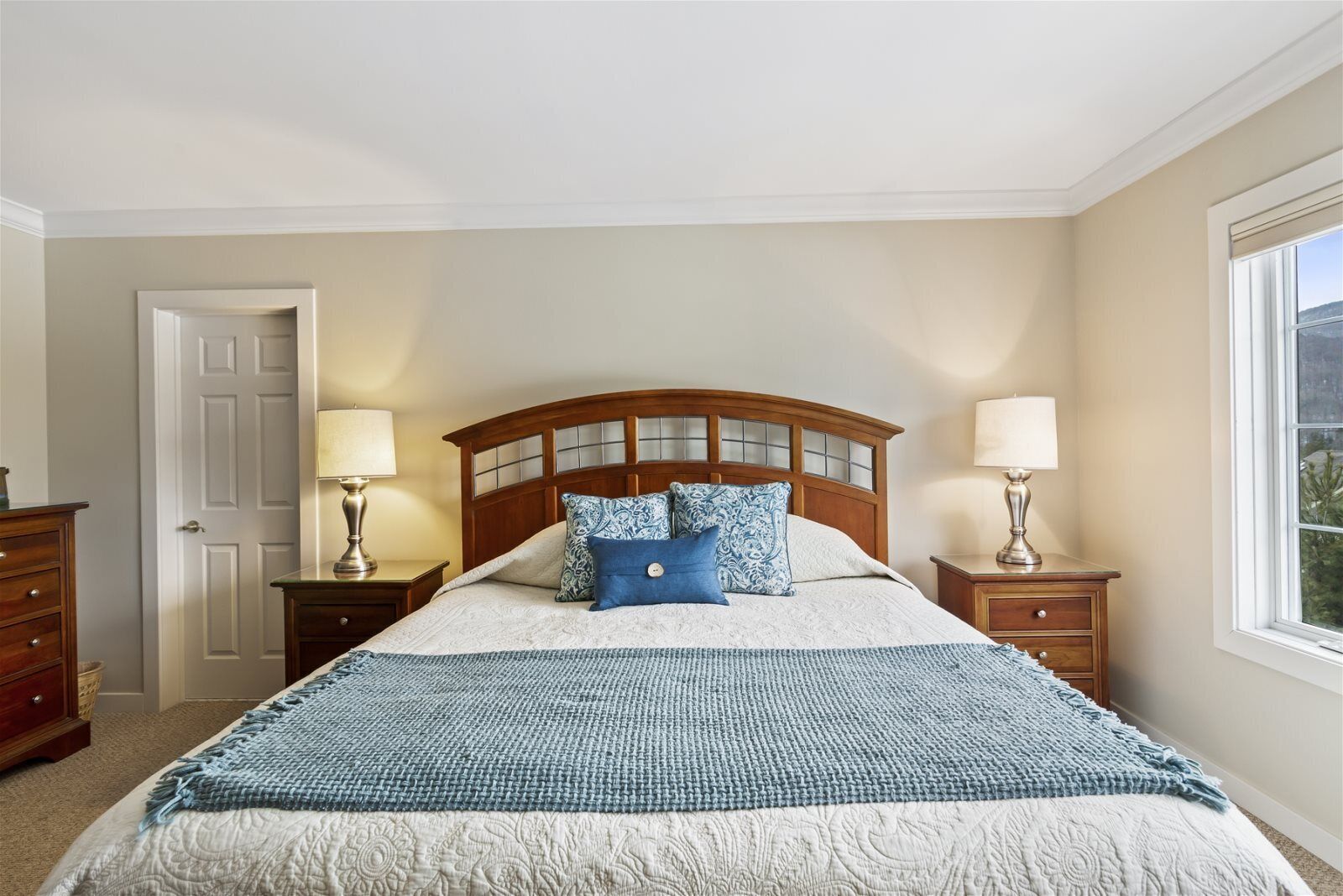 Un dormitorio con una cama grande, dos mesitas de noche con lámparas, un cabecero de madera y una puerta.