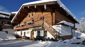 Un edificio de madera con techo inclinado cubierto de nieve, una escalera que lleva a un balcón y un letrero que indica un restaurante.