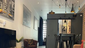 A modern living room with a flat-screen TV, a leather sofa, a dining area with a table and chairs, and a large window with curtains. - Montmartre Moulin rouge Batignolles (Paris)