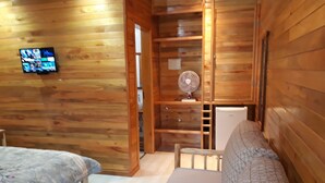 Habitación de cabaña de madera con una cama, un televisor y un ventilador.