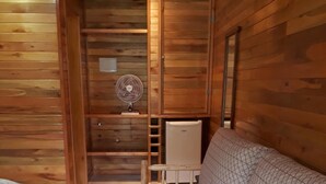 Una habitación tipo cabaña de madera con una cama, un ventilador y un refrigerador.