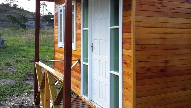 Una cabaña de madera con un porche, una puerta con paneles de vidrio y un pequeño espacio al aire libre.