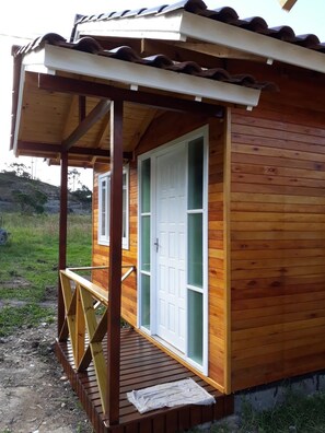 Una cabaña de madera con un porche, una puerta con paneles de vidrio y un pequeño espacio al aire libre.