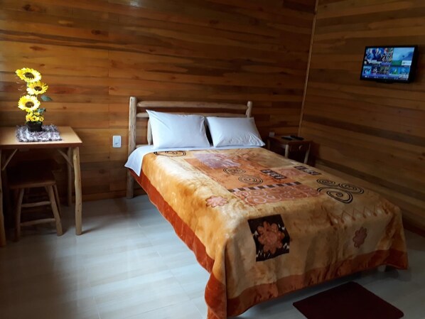 Una habitación con paneles de madera, una cama, un escritorio y un televisor en la pared.