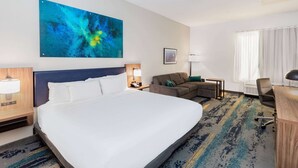 Quarto de hotel com uma cama grande, um sofá, uma escrivaninha e um quadro na parede.