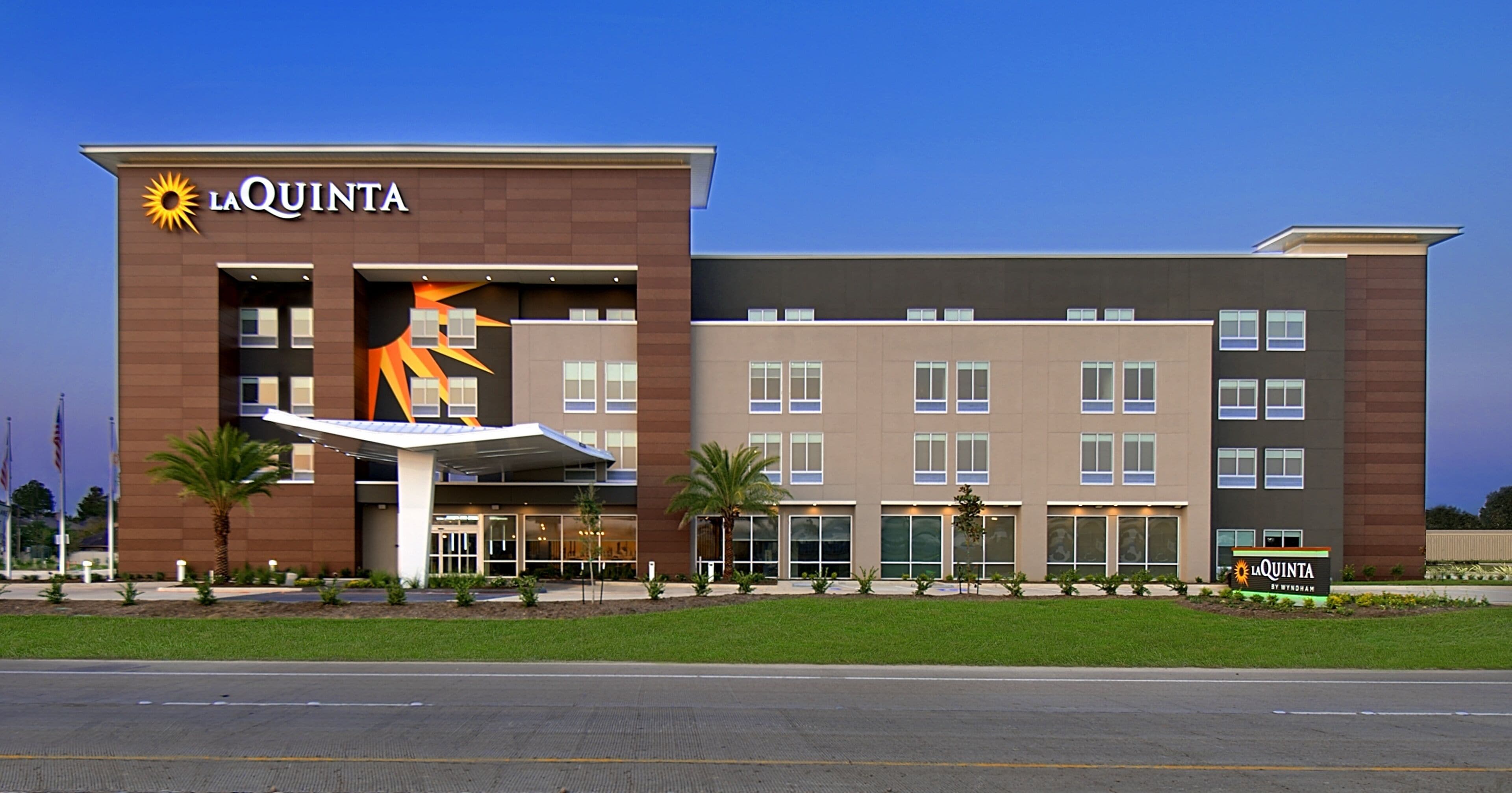 A La Quinta hotel with a modern design, featuring a prominent sun logo, a covered entrance, and a well-maintained lawn.