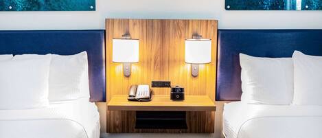 A hotel room with two beds, a wooden headboard, bedside lamps, a telephone, and a digital clock.