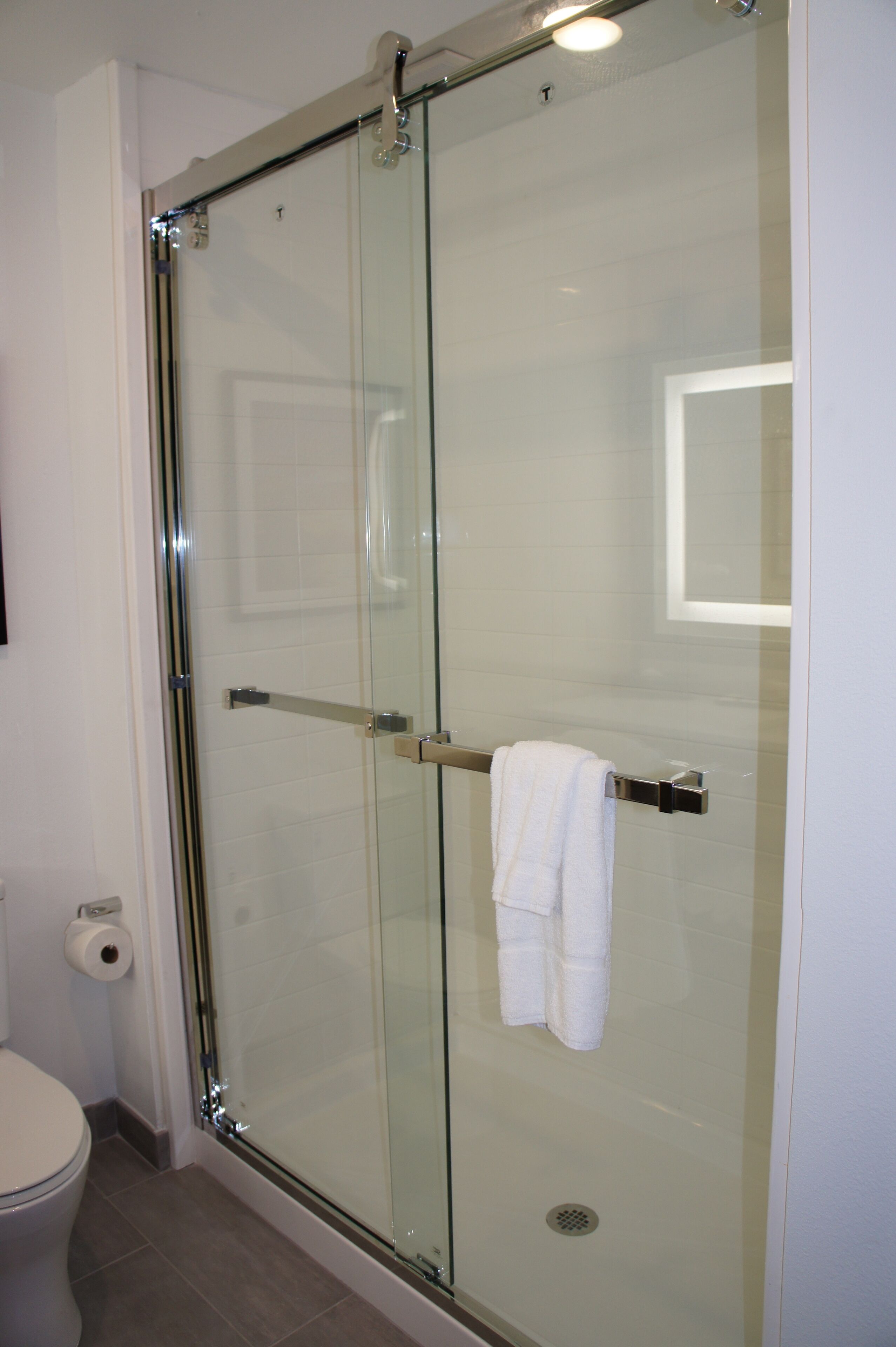 A glass-enclosed shower with a towel rack and a toilet visible to the left.