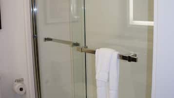 Une douche fermée par des parois de verre, avec un porte-serviettes et des toilettes visibles sur la gauche.