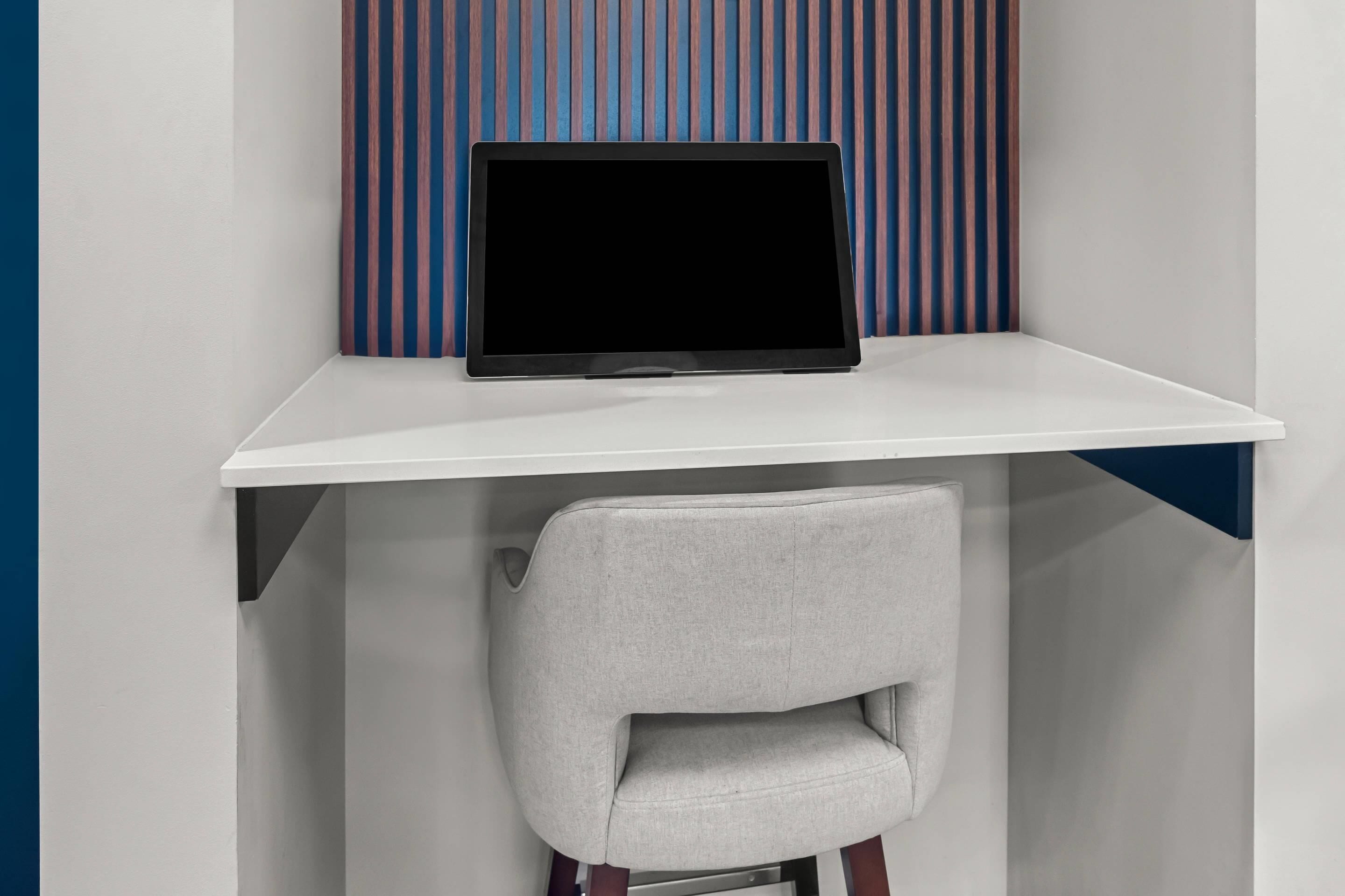 Un espacio de trabajo moderno con una tableta sobre un escritorio blanco, una silla gris y una pared a rayas de fondo.