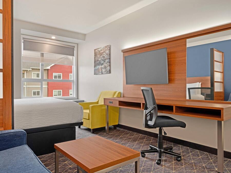 Een moderne hotelkamer met een bed, bureau, stoel, een klein tafeltje, een televisie en een raam met uitzicht op gebouwen.