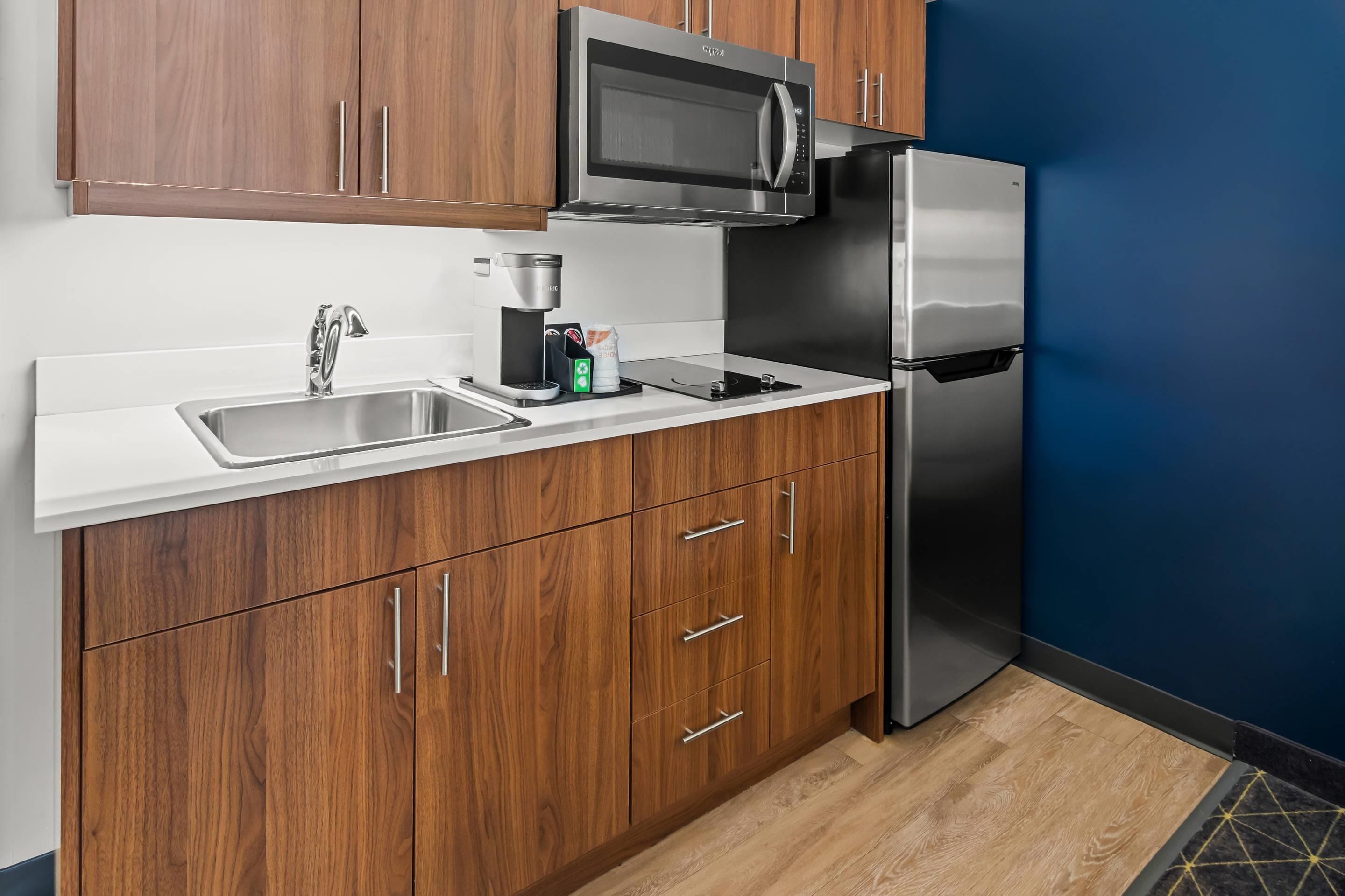 A modern kitchen with wooden cabinets, a stainless steel refrigerator, and a built-in microwave.