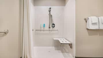 A shower area with a showerhead, a shelf with toiletries, and a towel rack.