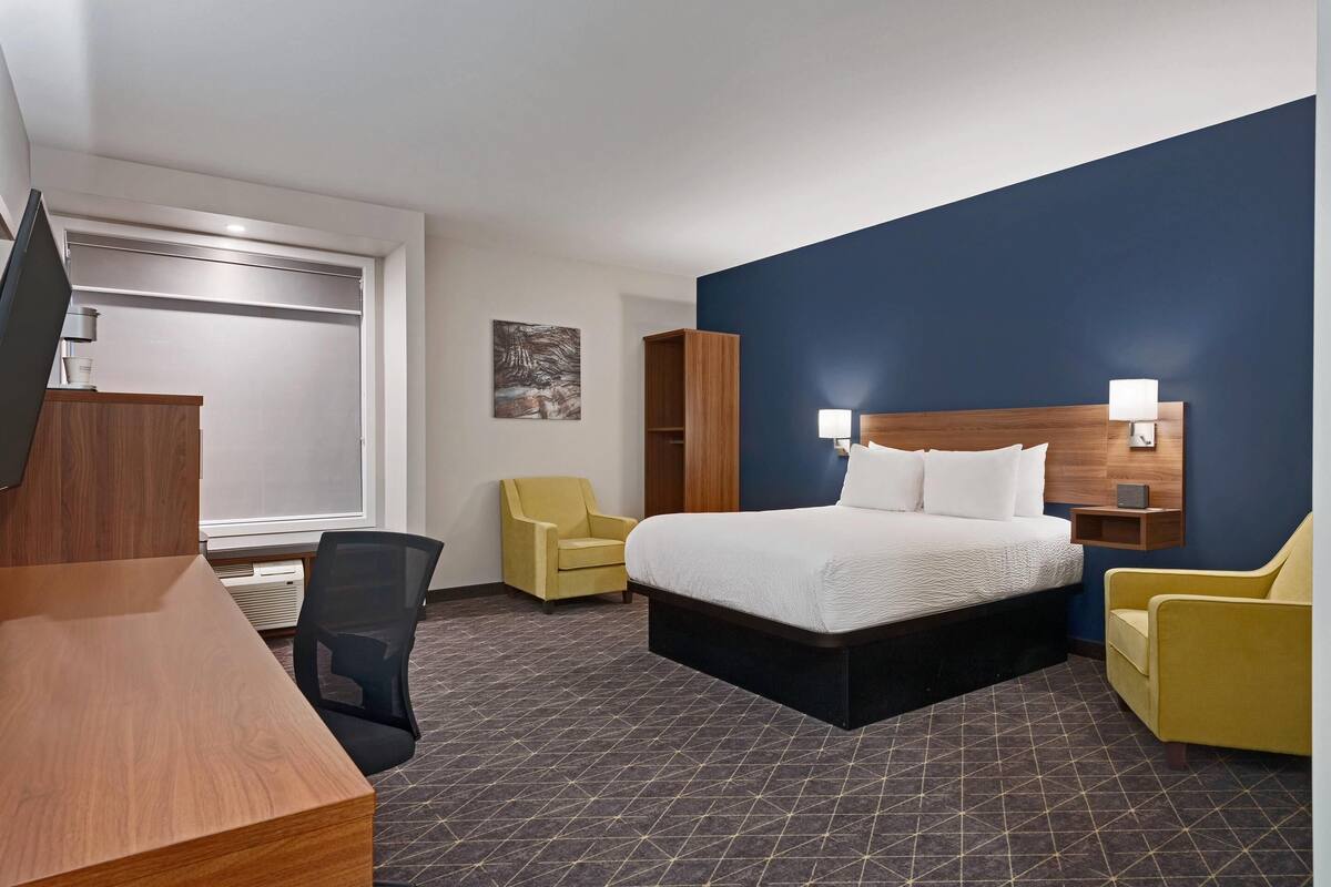 A hotel room with a bed, a desk, a chair, a wardrobe, and a wall-mounted TV.