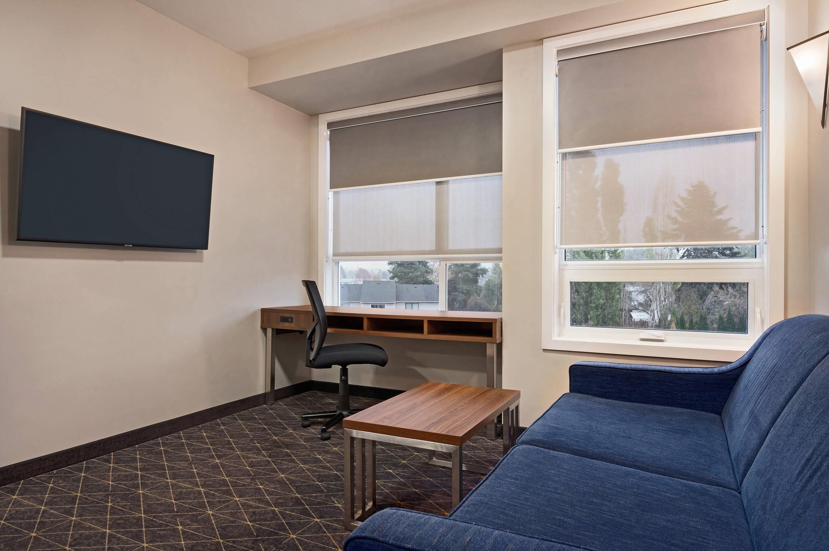 A room with a large window, a desk, a chair, a TV, and a blue sofa.