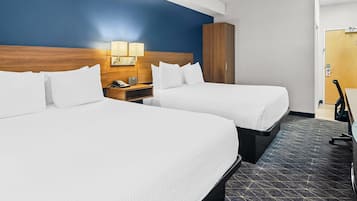 Habitación de hotel con dos camas, cabecero de madera, mesita de noche con lámpara y armario.