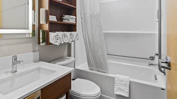 A modern bathroom with a white sink, toilet, and bathtub. There is a wooden shelf with towels and toiletries.