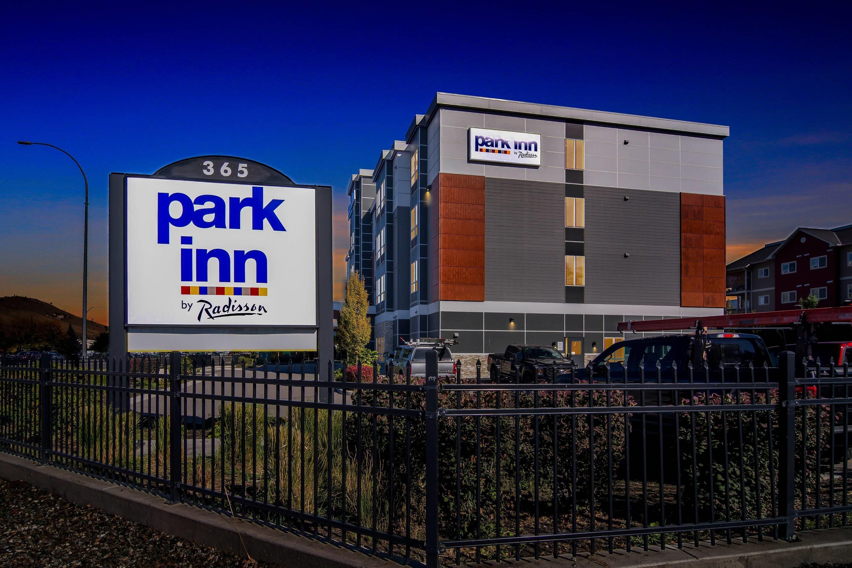 Un hotel Park Inn con un diseño moderno, un cartel llamativo y un área de estacionamiento cercada.