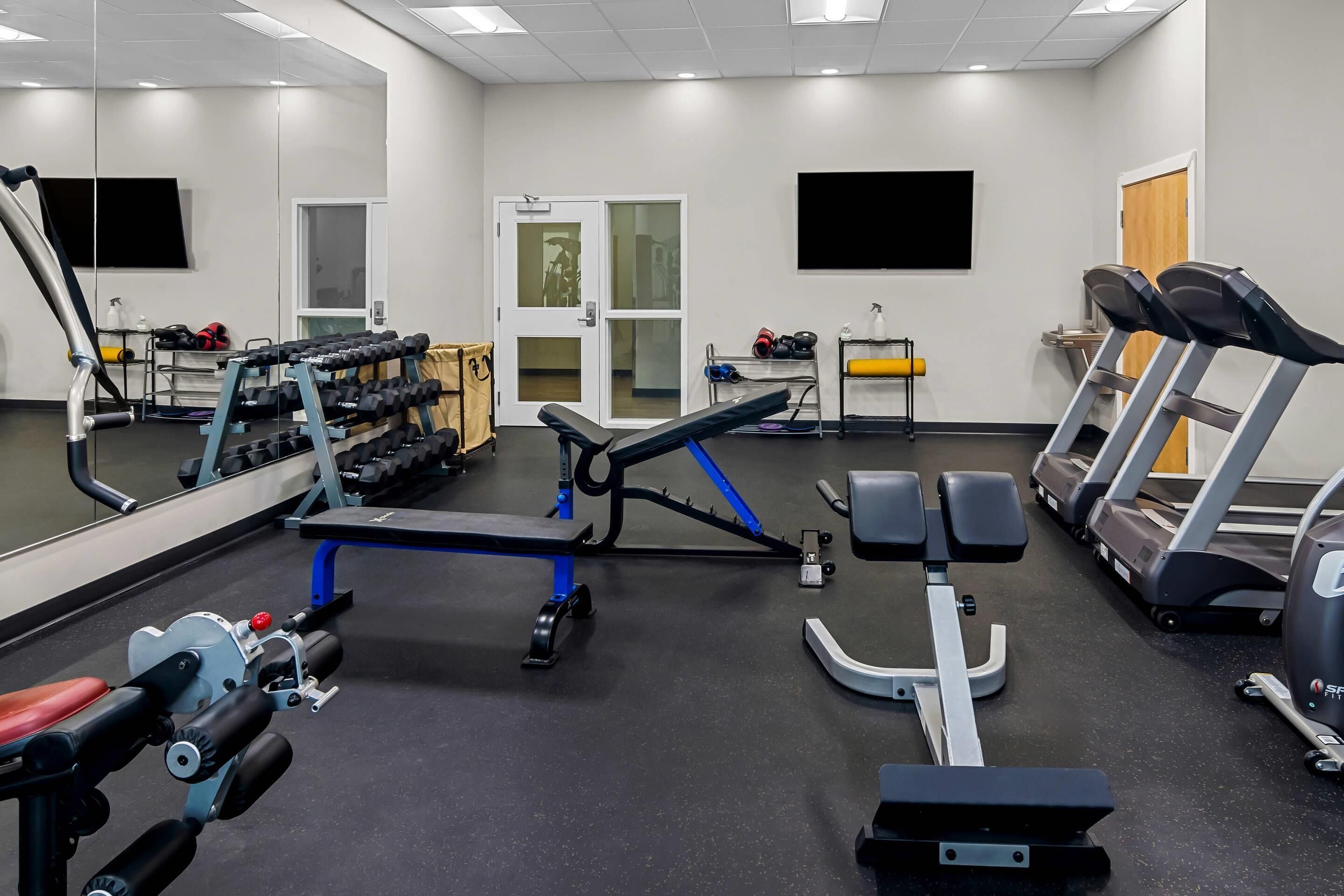 Et fitnesscenter med forskellig træningsudstyr, herunder håndvægte, en bænkpres og løbebånd.