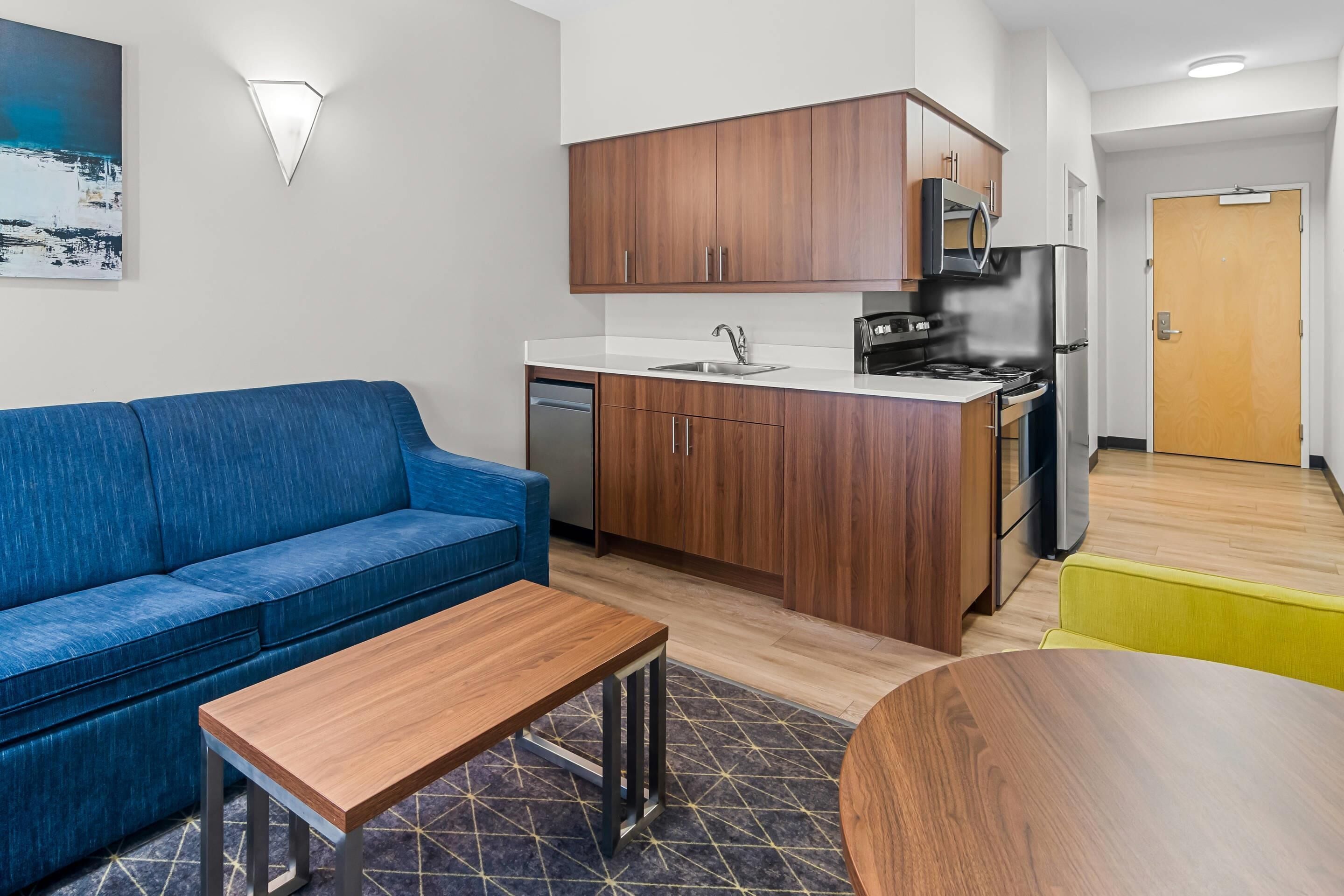 Un apartamento moderno con kitchenette, un sofá azul, una mesa de madera y una silla amarilla.
