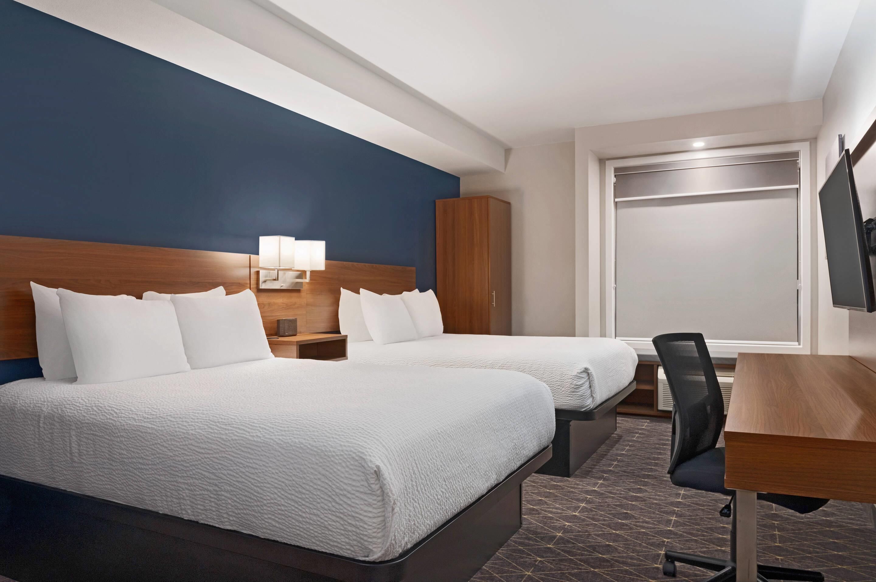 A hotel room with two beds, a desk, a chair, a wardrobe, and a TV.
