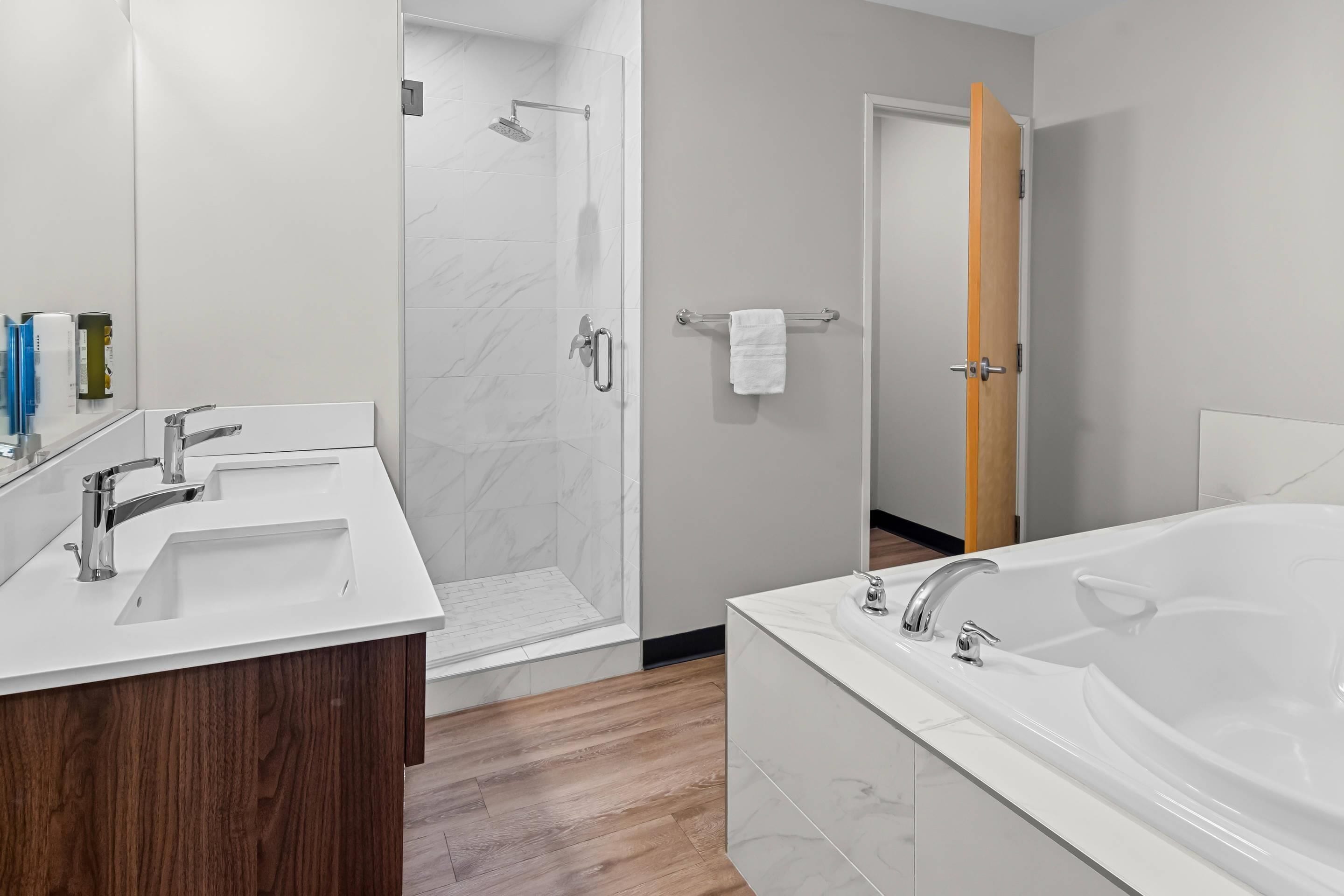 Un bagno moderno con una vasca da bagno spaziosa, due lavabi, una doccia e un mobile bagno in legno.
