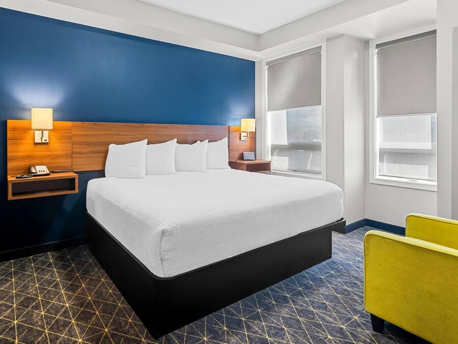 A hotel room with a large bed, a nightstand, a lamp, and a window with blinds.