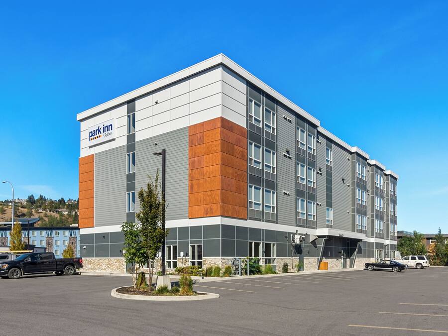 A modern hotel with a flat roof, large windows, and a parking lot.