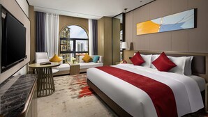Habitación de hotel moderna con una cama grande, televisión, zona de estar con mesa y vistas a la ciudad a través de un ventanal amplio.