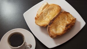 Un piatto bianco con due fette di pane tostato e una tazza di caffè su una superficie scura.