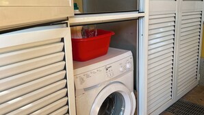 A compact laundry room with a front-loading washing machine and a red plastic basin.