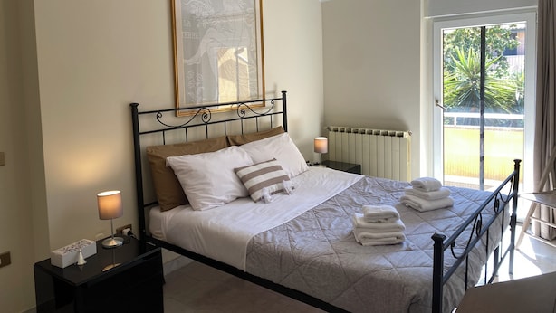A neatly made bed with white and striped pillows, a bedside lamp, and a framed artwork on the wall.