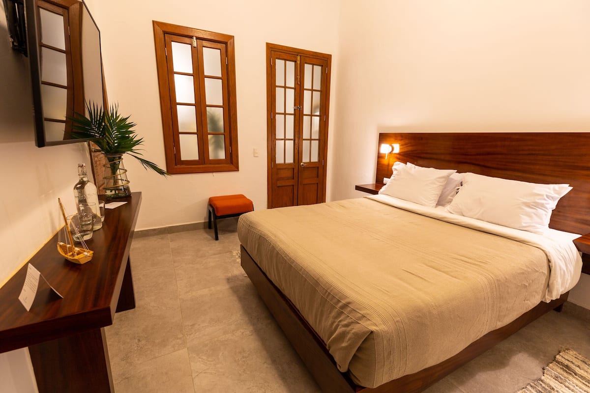 A bedroom with a wooden bed, a nightstand, a bedside table, a mirror, and two windows with wooden frames.