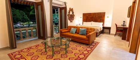 A hotel room with a bed, a sofa, a glass coffee table, and a view of the outdoors.