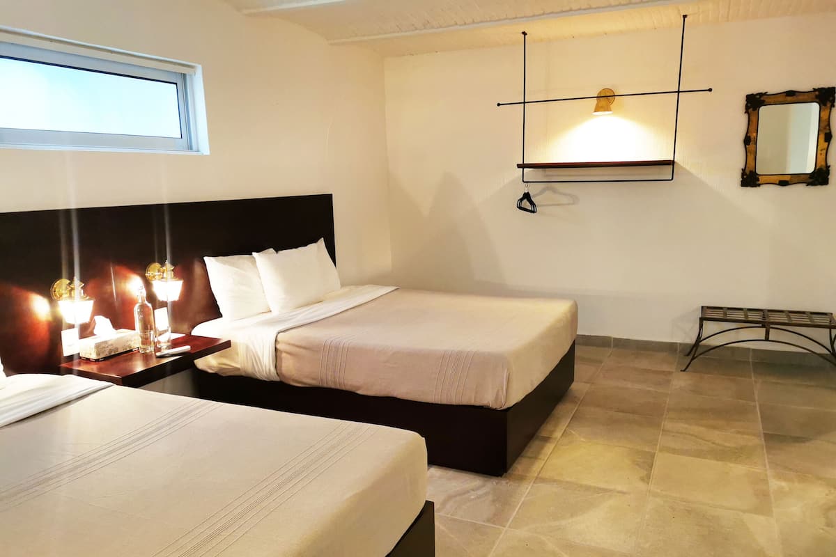 A hotel room with two beds, a nightstand with a lamp, a mirror, and a window.