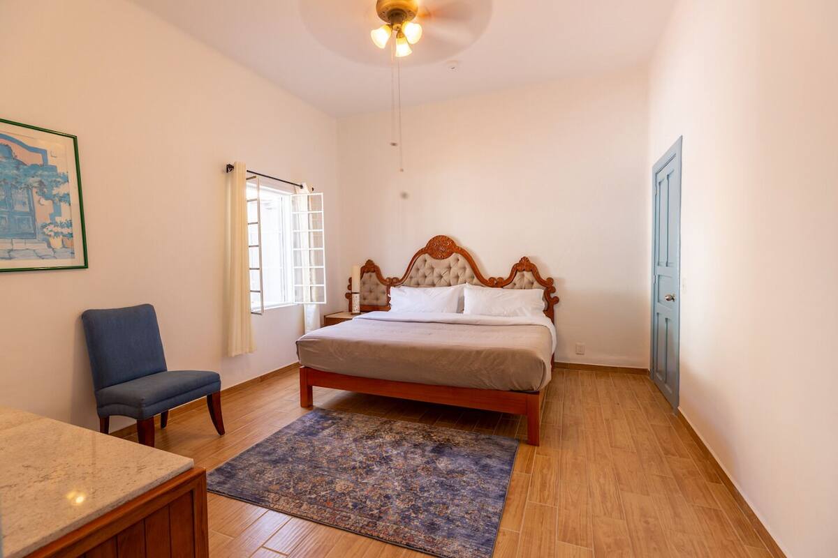 A bedroom with a bed, a chair, a small table, and a window.