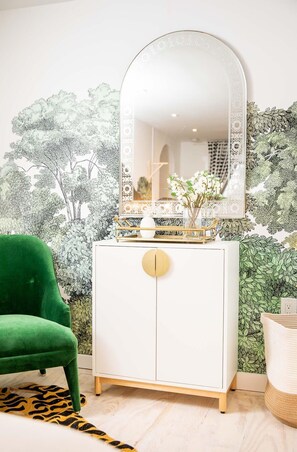 A room with a white cabinet, a green chair, and a mirror with a decorative frame.