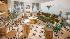 Un salon chaleureux avec un canapé vert, un tapis à motifs, des meubles en bois et une fresque murale.