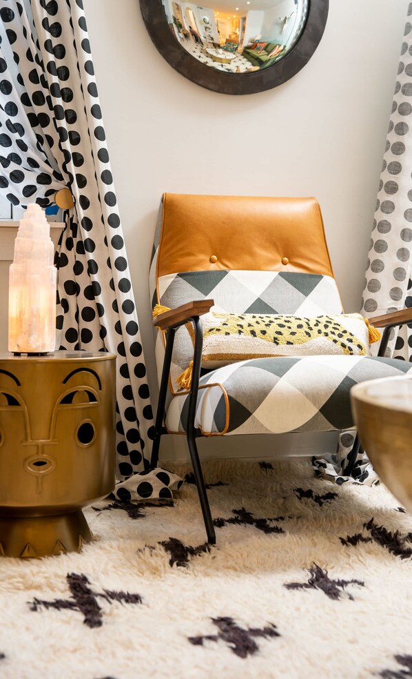 A cozy room with a patterned chair, a fluffy rug, and a round mirror on the wall.