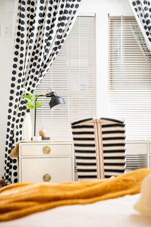 Une chambre à coucher avec un lit, une table de chevet avec une lampe, une chaise à rayures et une fenêtre avec des stores.
