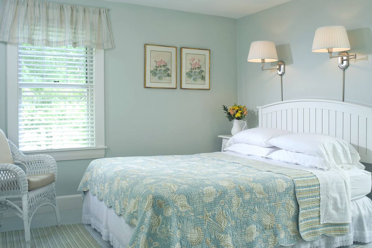 A bedroom with a bed, a chair, a nightstand, two wall-mounted lamps, and two framed pictures.
