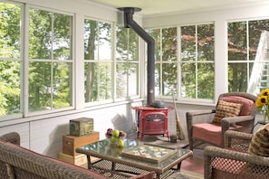 Relax in a traditional room with a large window overlooking lush greenery, a vintage stove, and wicker furniture.