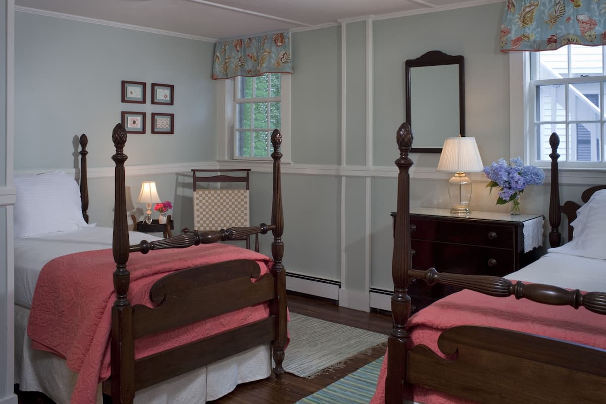 A bedroom with two wooden beds, a nightstand with a lamp, a dresser, and a mirror.