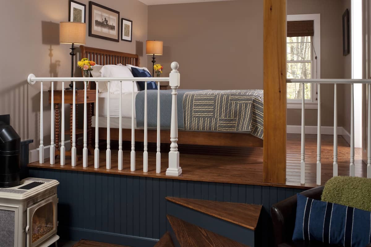 A bedroom with a wooden bed, a nightstand with lamps, a dresser, and a view of the outside.