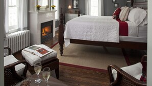 A bedroom with a large bed, a fireplace, a nightstand, and a window with curtains. - Newcastle Inn (Newcastle)